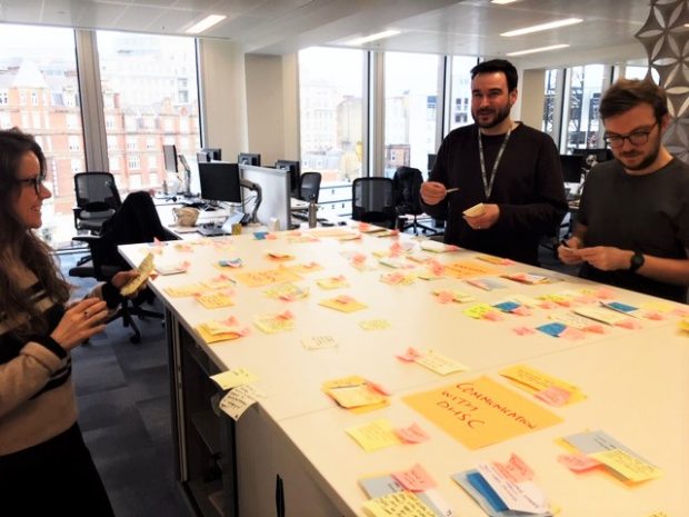 3 people stood around a table with post it notes