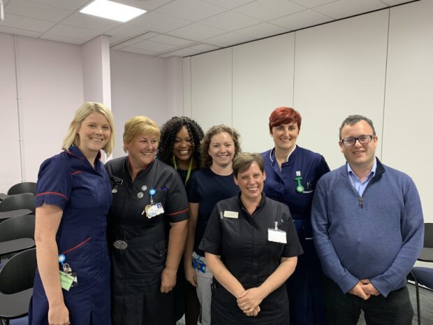 Six female NHS staff stand with Matthew Gould in a meeting room