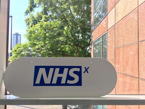 An NHSX sign on a window sill with a tree in the background